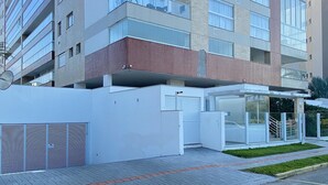A modern multi-story building with a glass facade, a covered entrance, and a parking area with a brick pathway. - Cobertura com Jacuzzi em Palmas  (Governador Celso Ramos)