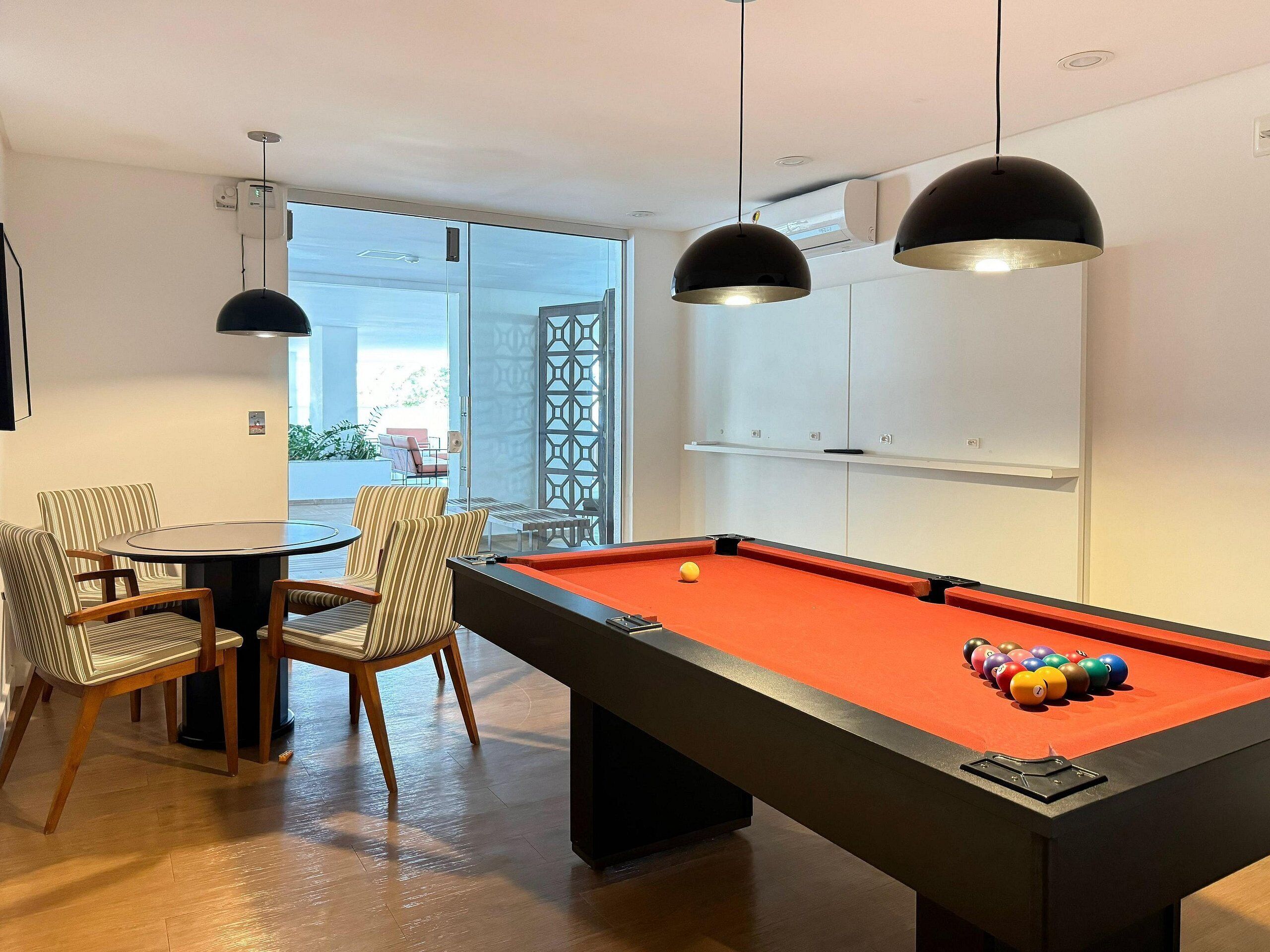 A pool table with a red felt surface, surrounded by striped chairs and a small round table.