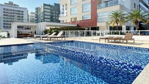 A swimming pool with tiled blue mosaic flooring, surrounded by lounge chairs and a covered seating area. - Cobertura com Jacuzzi em Palmas  (Governador Celso Ramos)