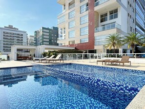 A swimming pool with tiled blue mosaic flooring, surrounded by lounge chairs and a covered seating area.