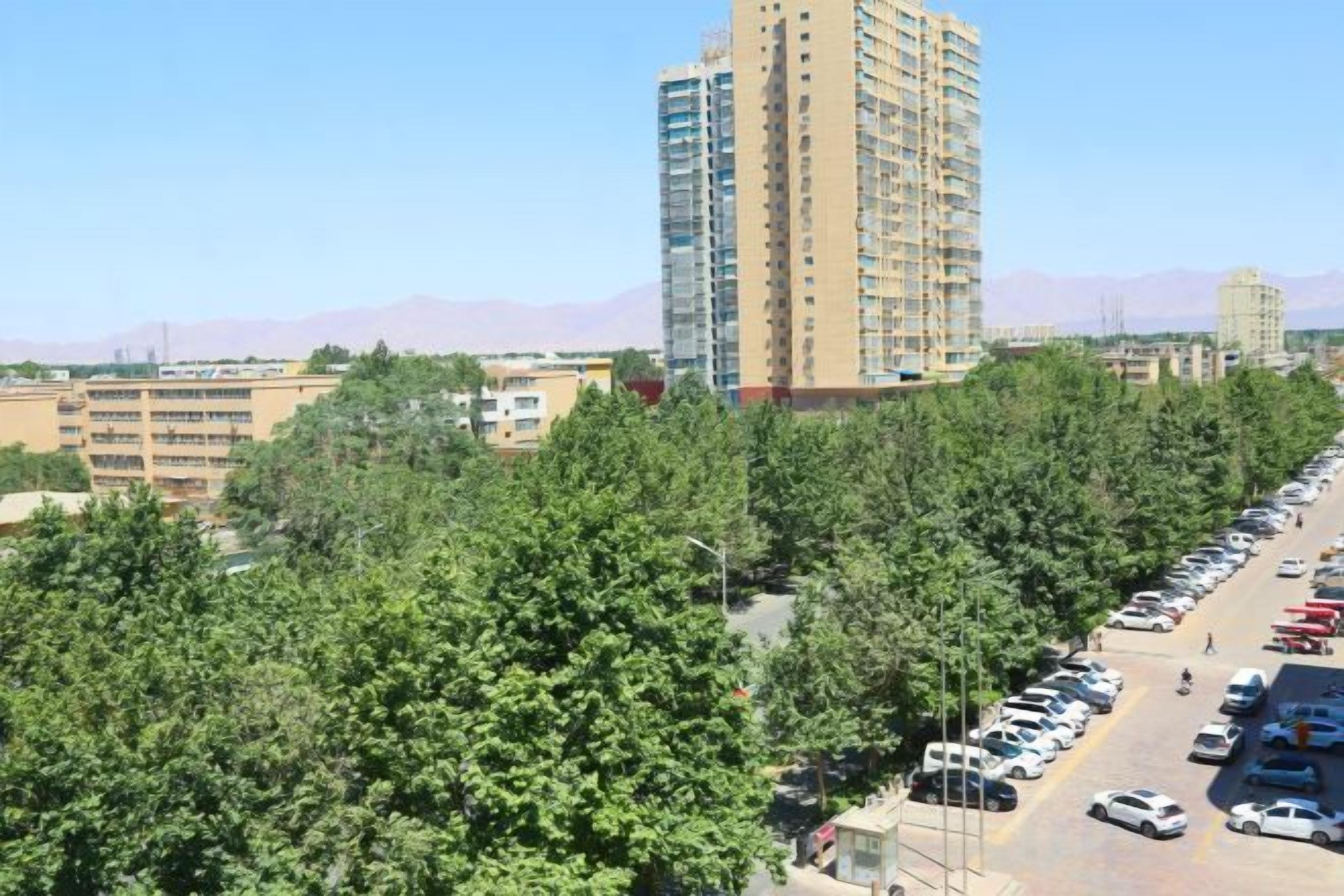 A high-rise building with multiple floors, surrounded by a parking area and dense greenery.