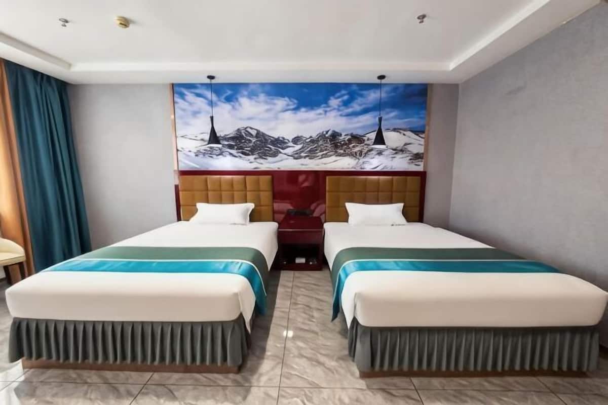 A hotel room with two beds, a large window, a mural of mountains, and a wooden headboard.