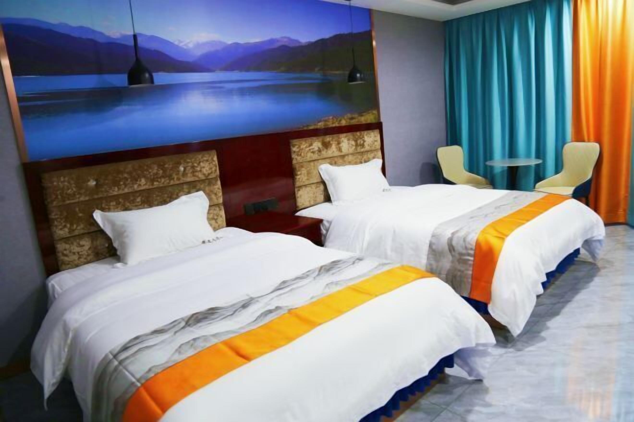 Habitación de hotel con dos camas, un cuadro grande de un lago, una mesita pequeña y dos sillas.