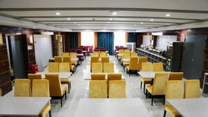 Un'ampia sala da pranzo con sedie gialle e tavoli bianchi, disposti in file.