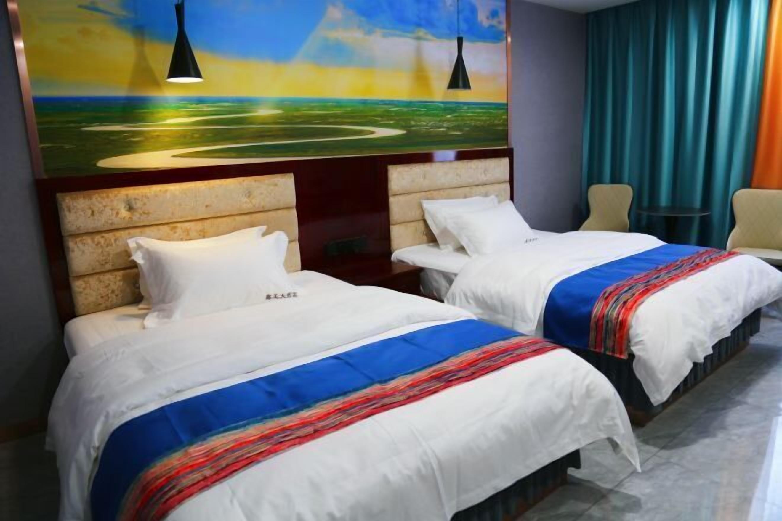 Una habitación de hotel con dos camas, cada una con una colcha blanca y una manta de colores. En la pared, sobre las camas, hay un cuadro de un paisaje.