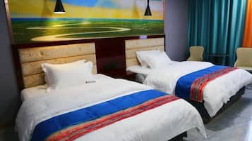 Una habitación de hotel con dos camas, cada una con una colcha blanca y una manta de colores. En la pared, sobre las camas, hay un cuadro de un paisaje.