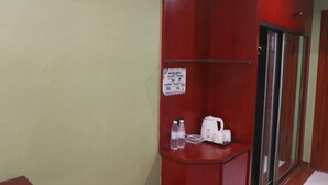 A hotel room with a wooden wardrobe, a small table with a kettle and water bottles, and a sign on the wall.
