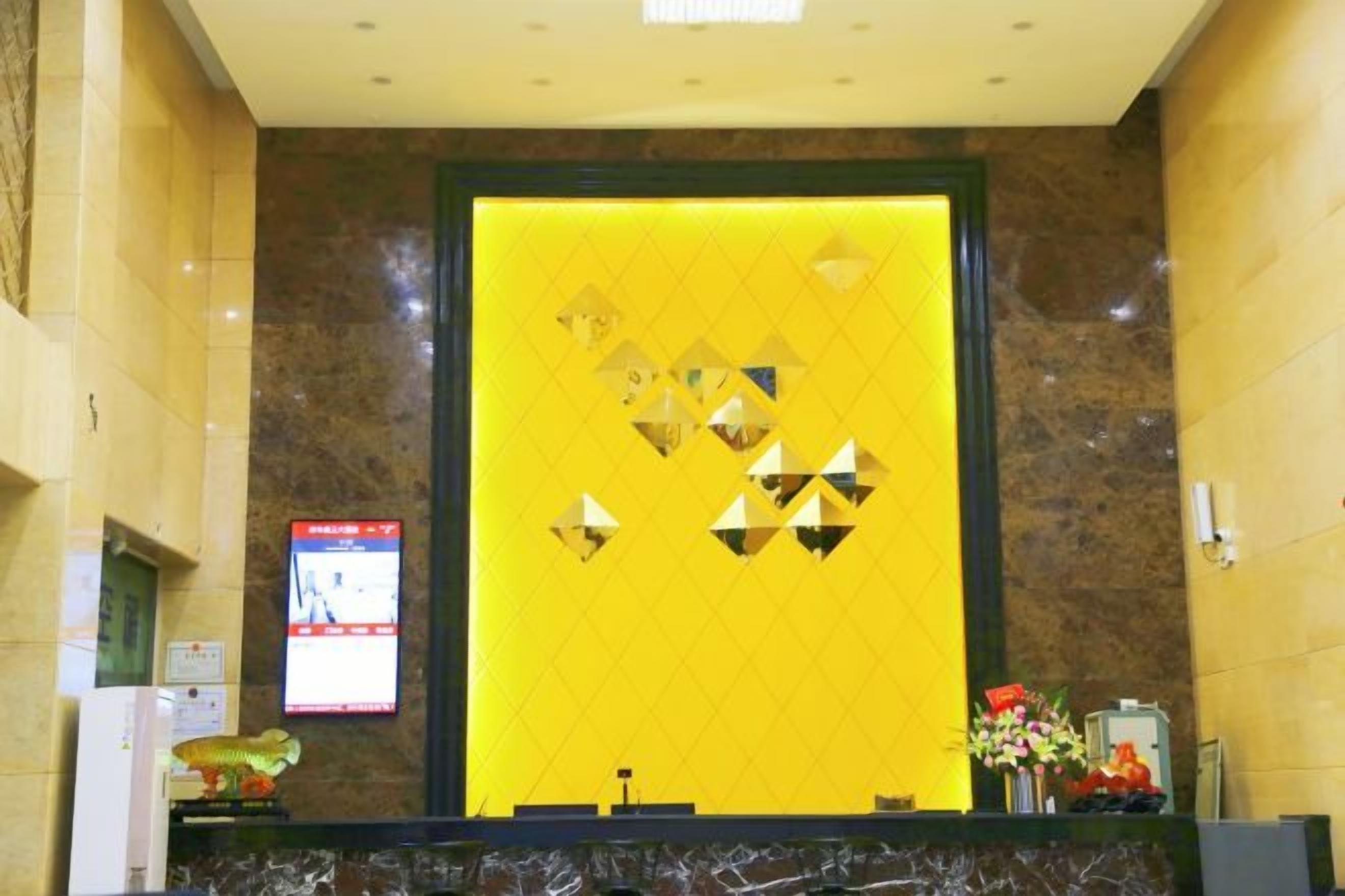 A reception area with a marble counter, a yellow wall with geometric patterns, and a digital screen displaying information.