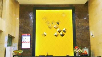 A reception area with a marble counter, a yellow wall with geometric patterns, and a digital screen displaying information.