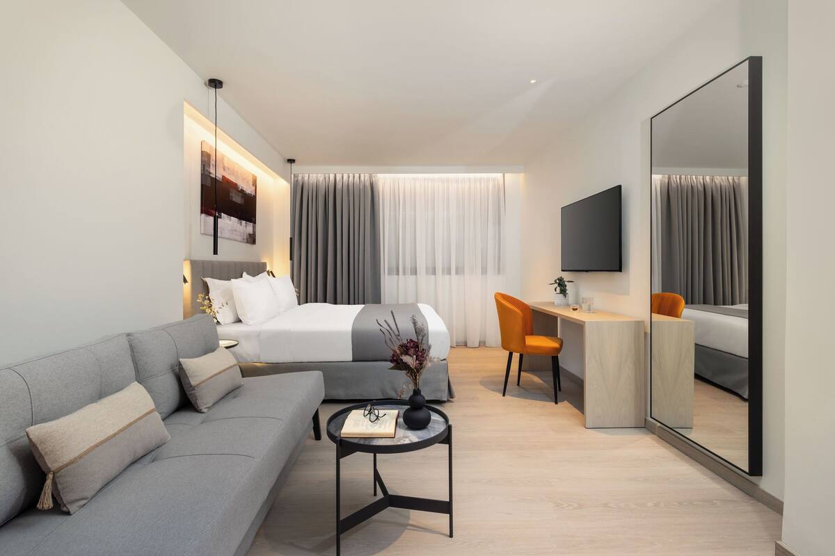 A modern hotel room with a sofa, a bed, a desk, and a TV.