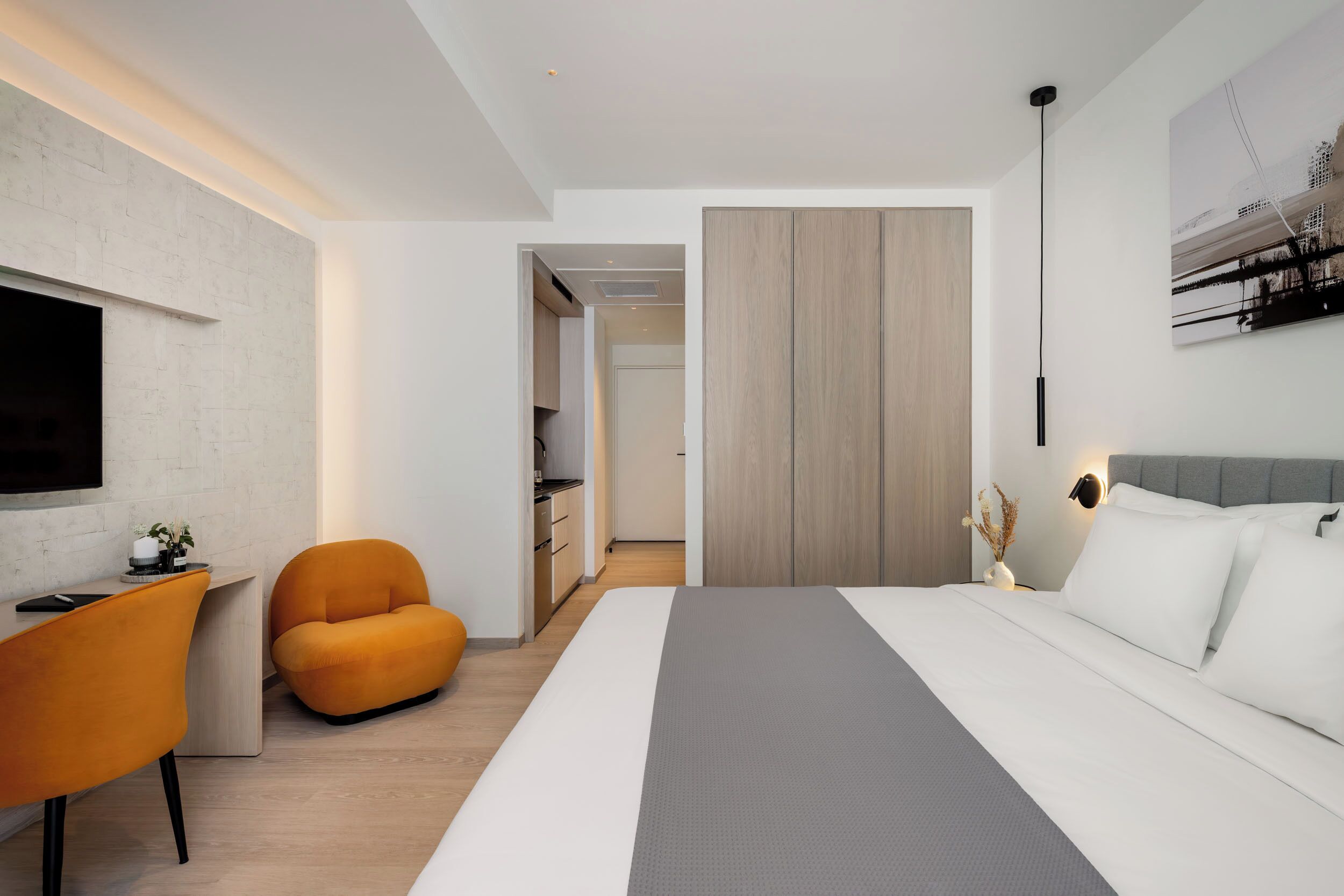 A modern bedroom with a large bed, a desk, an orange chair, and a wardrobe.