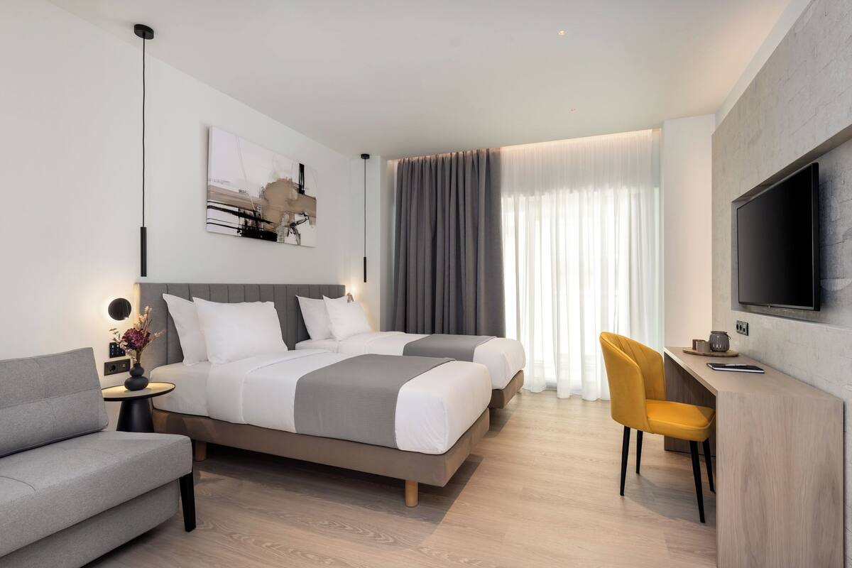 A modern hotel room with a bed, a sofa, a desk, and a TV.