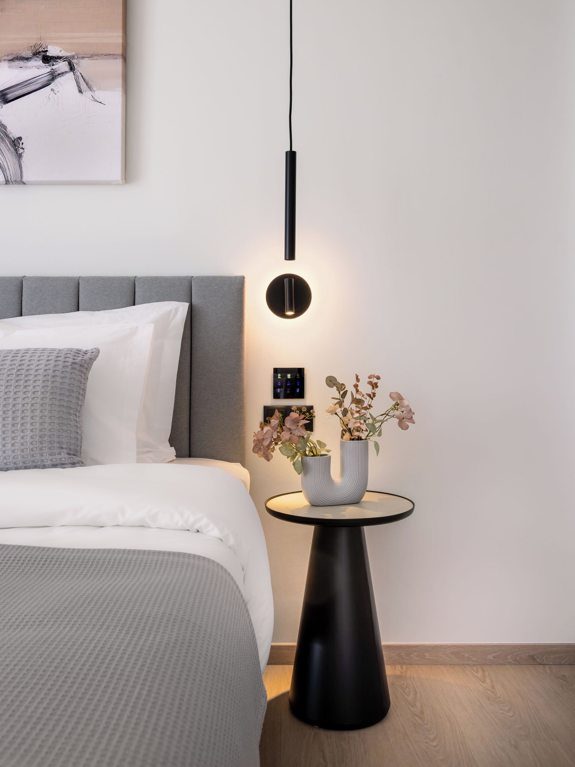 Ett modernt sovrum med en säng, ett sängbord och en väggmonterad lampa.