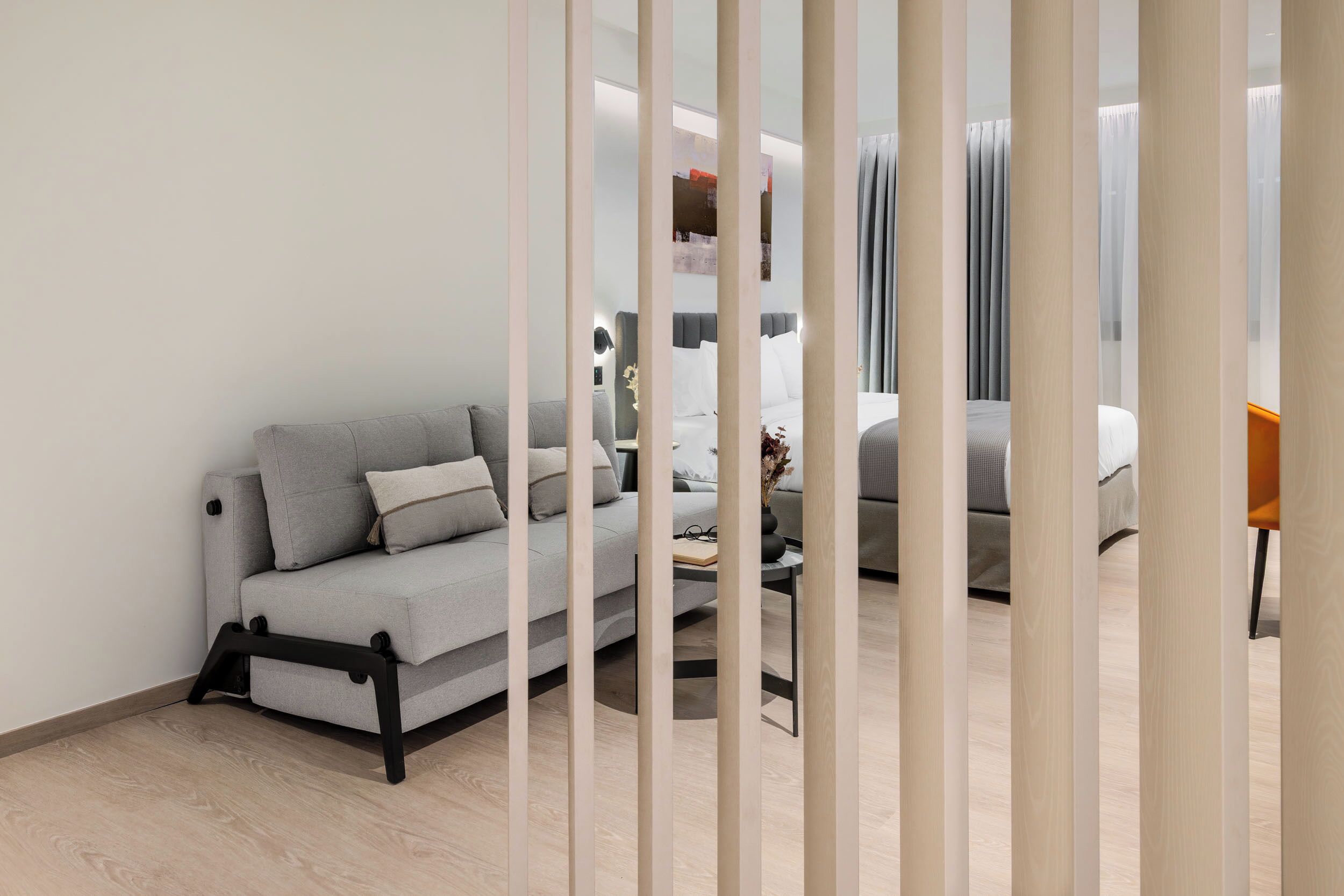 A modern hotel room with a grey sofa, a small table, and a bed with grey bedding.