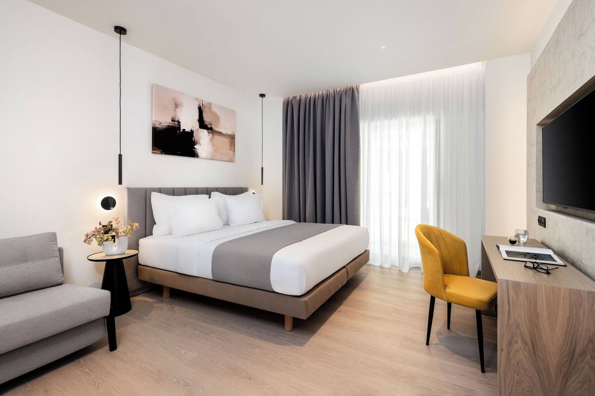 A modern hotel room with a bed, a sofa, a desk, and a TV.