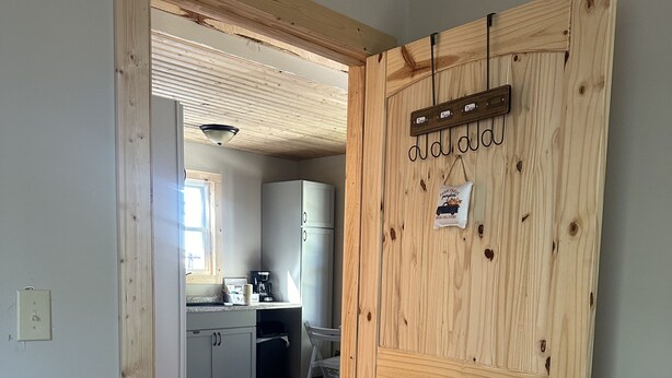 Een houten deur met een naambordje, een keuken met keukenkastjes en een koelkast, en een houten vloer.