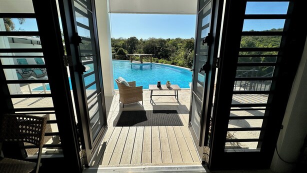 A view of a swimming pool with lounge chairs and a table, through open doors. - Dragonfly Hill Private Caribbean Escape w/private pool near Buye and Boqueron (Cabo Rojo)