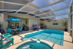 A covered outdoor swimming pool with lounge chairs and a table, surrounded by potted plants and a sign reading "Villa Serenita."