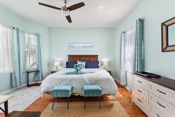 A bedroom with a bed, two bedside tables, a nightstand, a dresser, a ceiling fan, and a window with curtains.