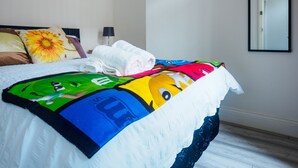 A neatly made bed with a colorful blanket, a pillow with a sunflower design, and a painting of a sunflower on the wall. - Couldon Lodge  Double Room 1 (Stoke-on-Trent)