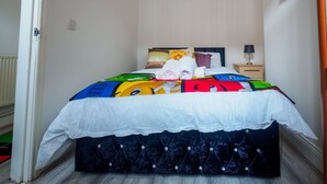 A bed with a colorful quilt, a bedside table with a lamp, and a door to the left. - Couldon Lodge  Double Room 1 (Stoke-on-Trent)