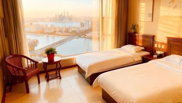 A hotel room with two beds, a chair, a small table with a plant, and a view of a cityscape and river.