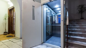 Une porte d’ascenseur ouverte donne sur un intérieur moderne avec un escalier.