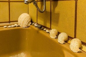 A bathtub with a yellowish-brown interior, surrounded by seashells and smooth stones. - Charming Apartment in Zadar With City Views (Zadar)