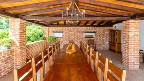 Un espacio de comedor al aire libre con techo, una mesa de madera larga y sillas, paredes de ladrillo y techo de madera.