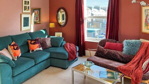 A living room with a teal sofa, a brown sofa, a coffee table, and a window with red curtains.