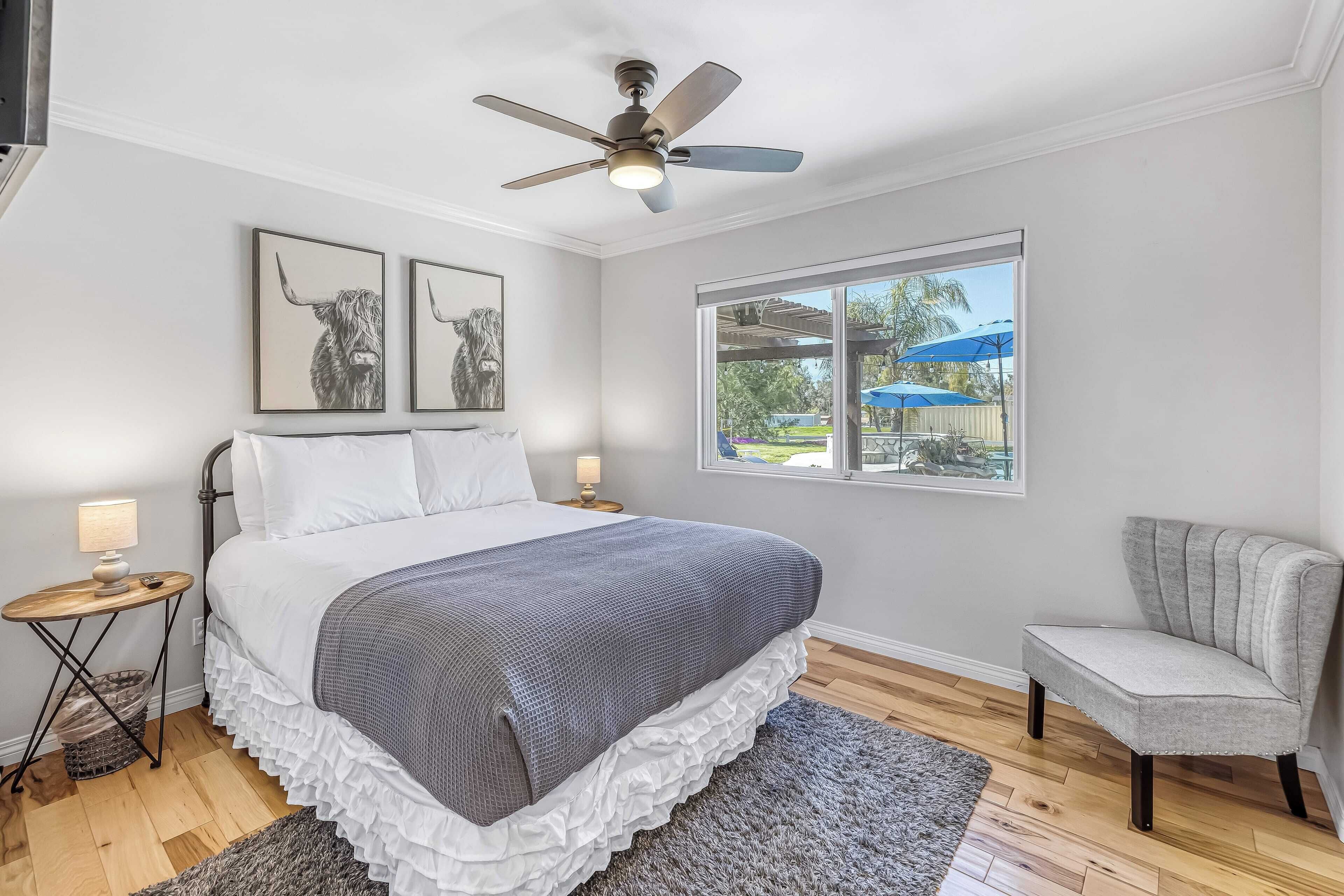 Un dormitorio con cama, ventilador de techo, ventana con vistas al exterior y una silla.