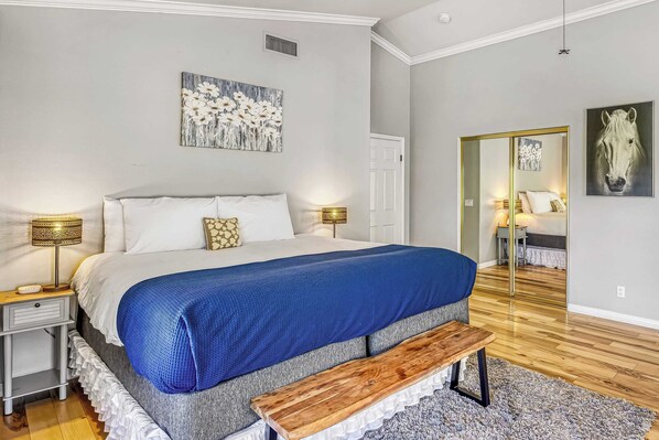 A bedroom with a bed, bedside lamps, a bench, a rug, and artwork on the walls.