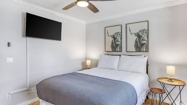 A bedroom with a bed, a mounted TV, two wall-mounted artworks, a ceiling fan, bedside lamps, and a small wooden side table. - Temecula Wine Country Home w/ Pool, Hot Tub, Game Room & Vineyard Views (Temecula)