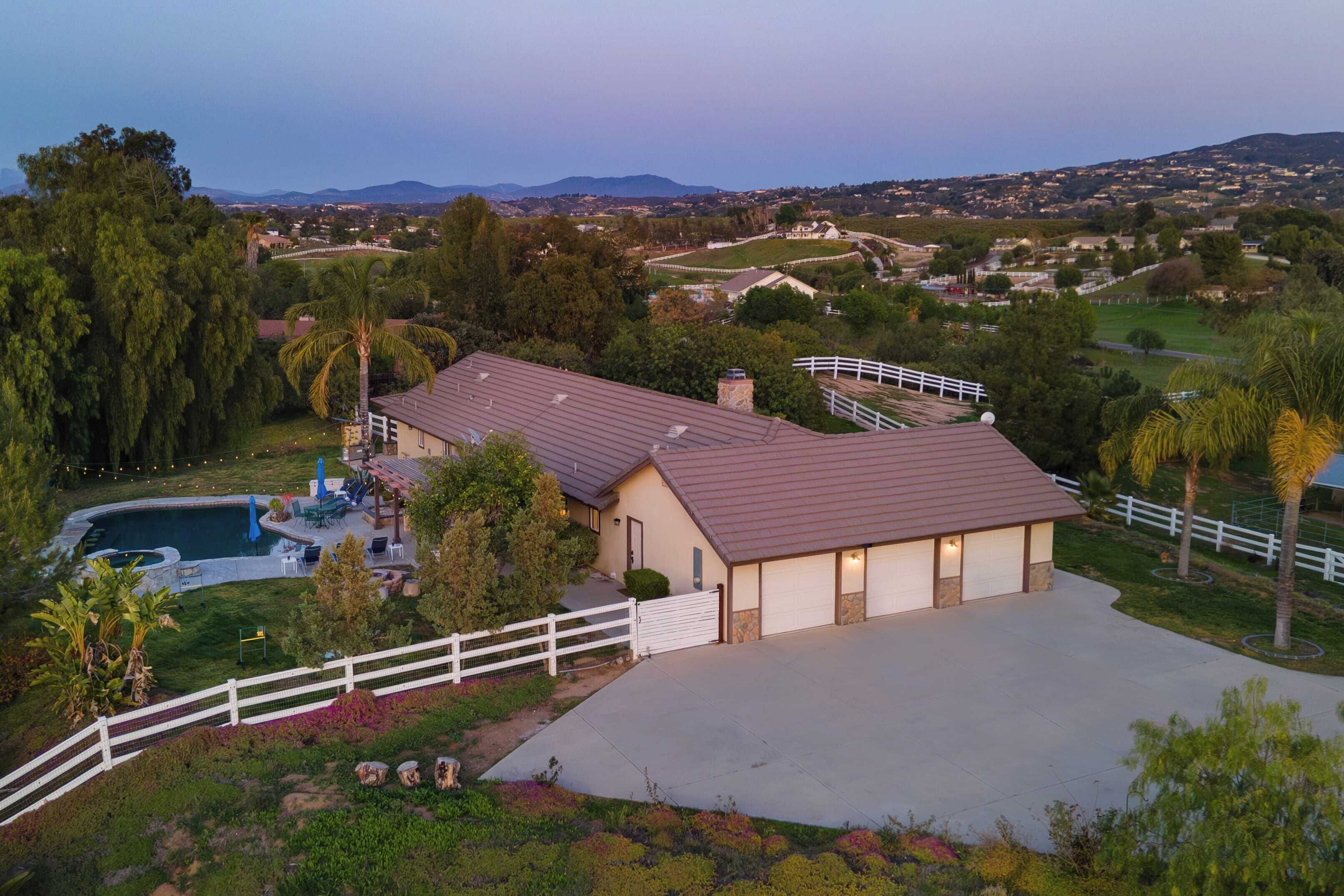 Una casa con un amplio camino de entrada, piscina y patio cercado.
