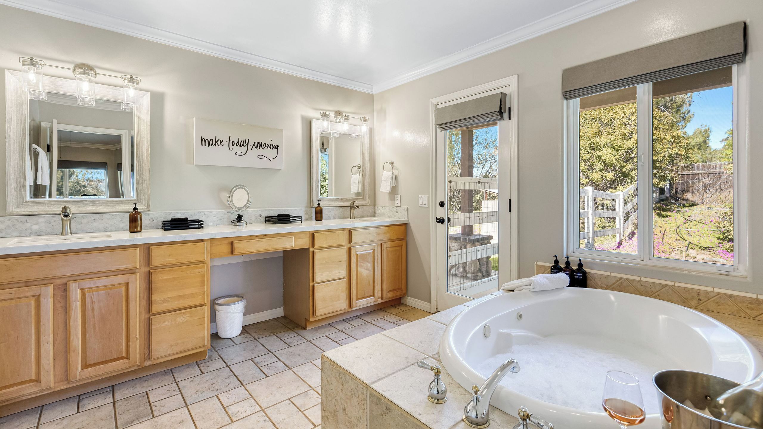 Une salle de bain spacieuse avec une grande baignoire, un meuble-lavabo avec un miroir et une vue sur un jardin par la fenêtre.