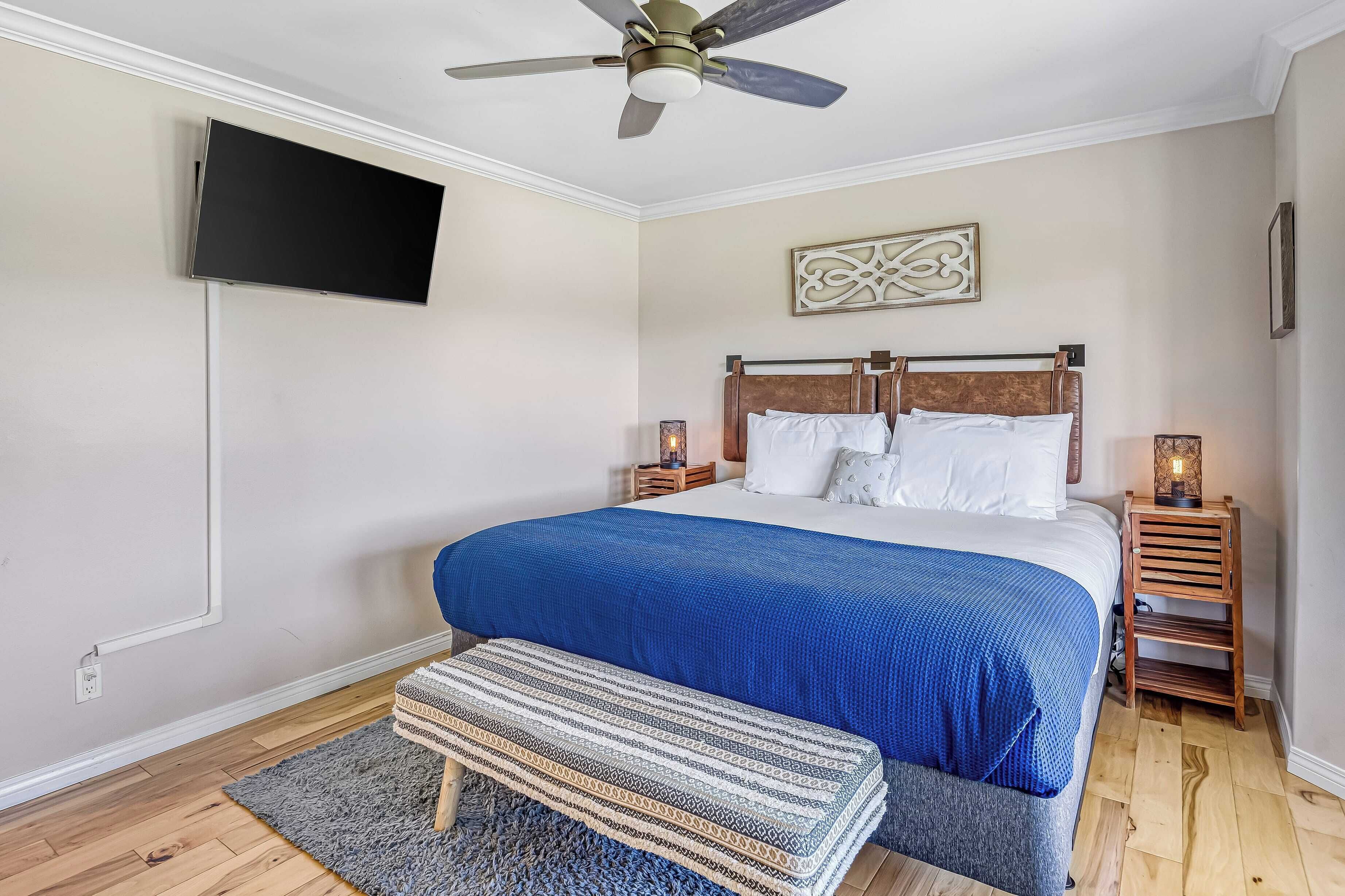 A bedroom with a bed, a bench, a ceiling fan, a TV, and a bedside table with a lamp.