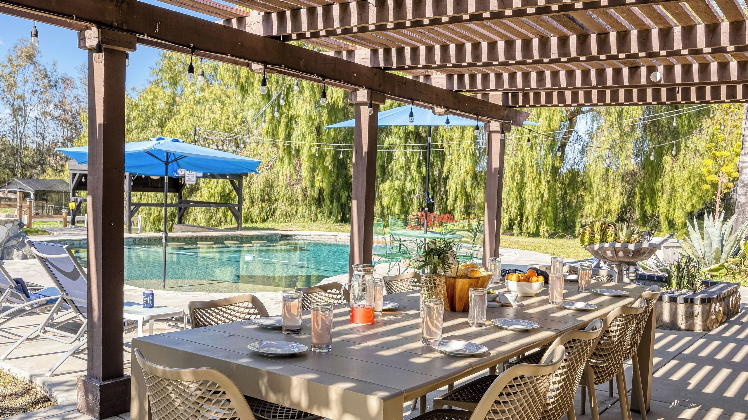 An outdoor pool area with a pergola, lounge chairs, and a table set for dining.