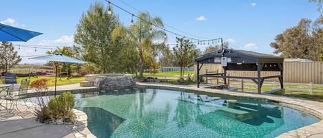 A backyard with a swimming pool, outdoor furniture, and a pergola.