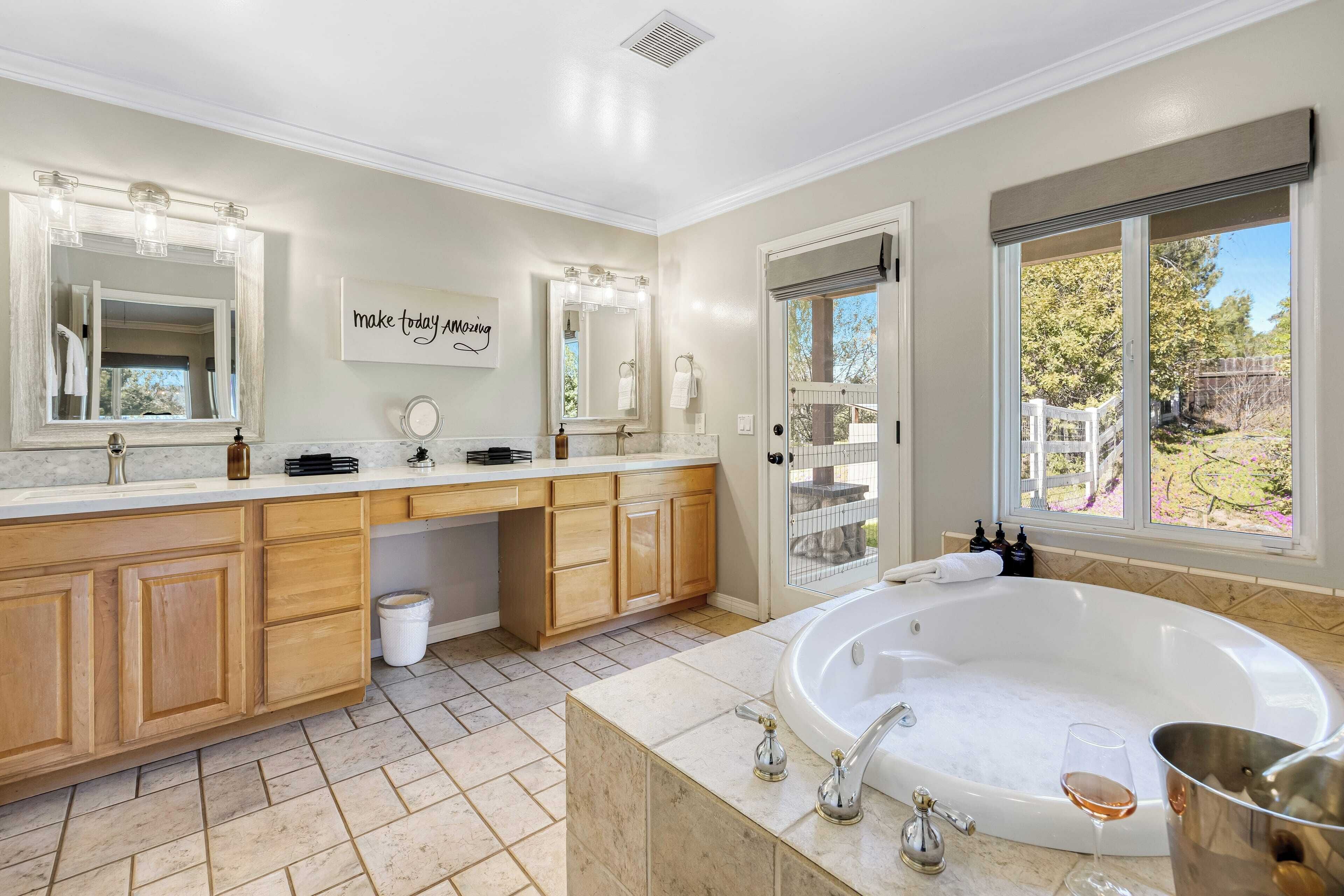 Une salle de bain spacieuse avec une grande baignoire, un meuble-lavabo double avec un miroir, et une vue sur le jardin arrière par une fenêtre.