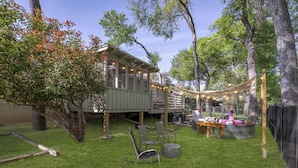 Patio trasero con terraza de madera, un parque infantil y una mesa con juguetes hinchables de colores.