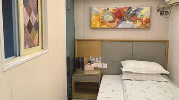 Ein Hotelzimmer mit Bett, Nachttisch, einem Gemälde und einem Fenster mit gemustertem Vorhang.