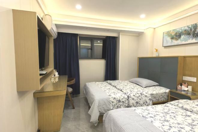 Ein Hotelzimmer mit zwei Betten, einem Schreibtisch, einem Stuhl, einem Fenster mit Vorhängen und einem Bild an der Wand.