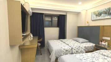 Ein Hotelzimmer mit zwei Betten, einem Schreibtisch, einem Stuhl, einem Fenster mit Vorhängen und einem Bild an der Wand.