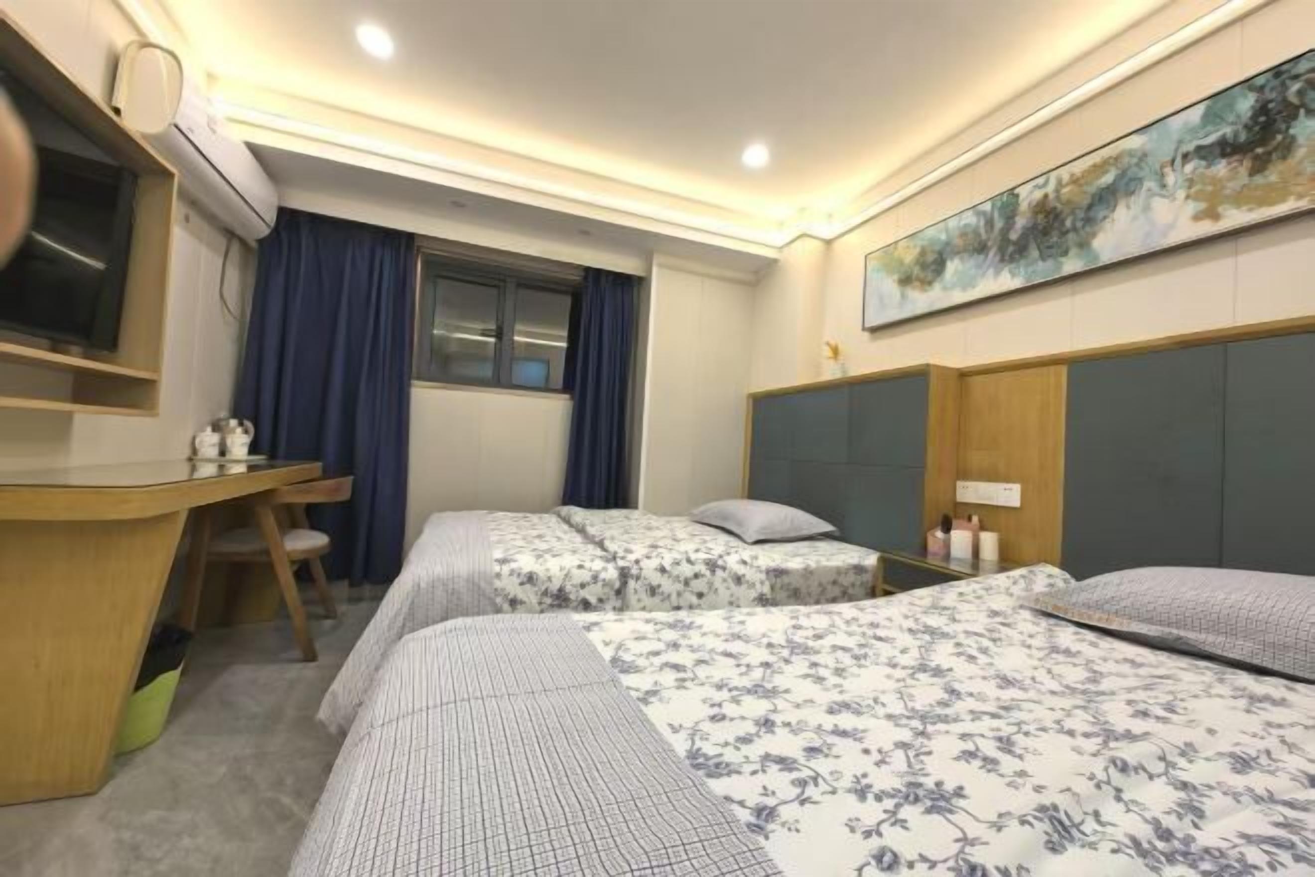 A hotel room with two beds, a desk, a chair, a TV, and a painting on the wall.