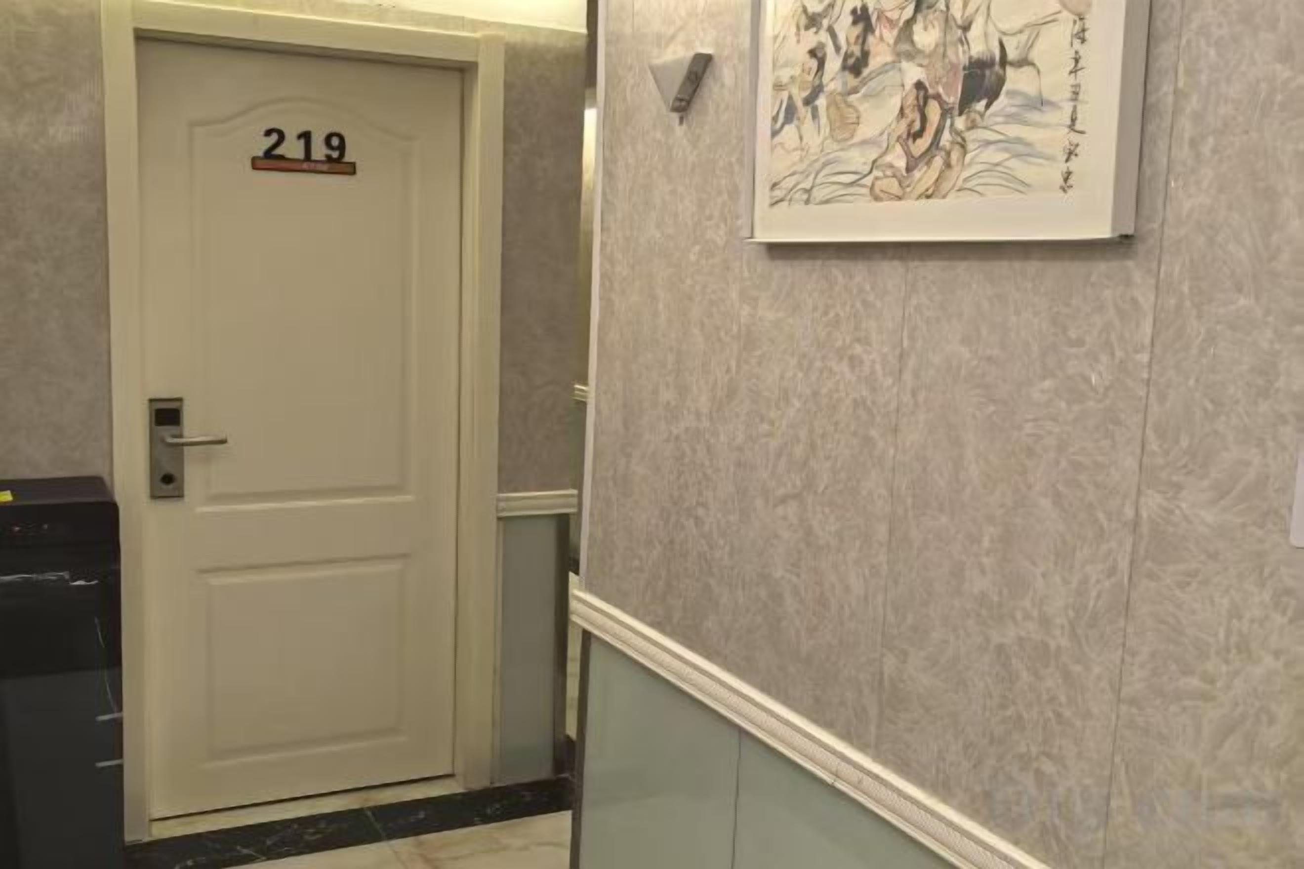 Een gang met een deur met het nummer '219' en een lijst met een kunstwerk aan de muur.