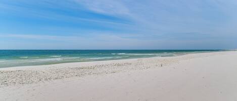 Ein weiter, sandiger Strand mit sanften Wellen und blauem Himmel.