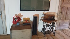 A wooden chest with a vase of red flowers, a vintage sewing machine on a table, and a television mounted on the wall. - Room-kungsgården BnB Room 1 (Kungsgarden)