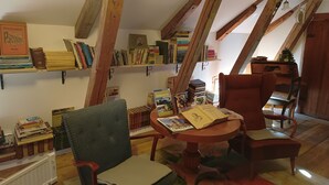 A cozy attic room with exposed wooden beams, a round wooden table, two chairs, and a bookshelf filled with books. - Room-kungsgården BnB Room 1 (Kungsgarden)