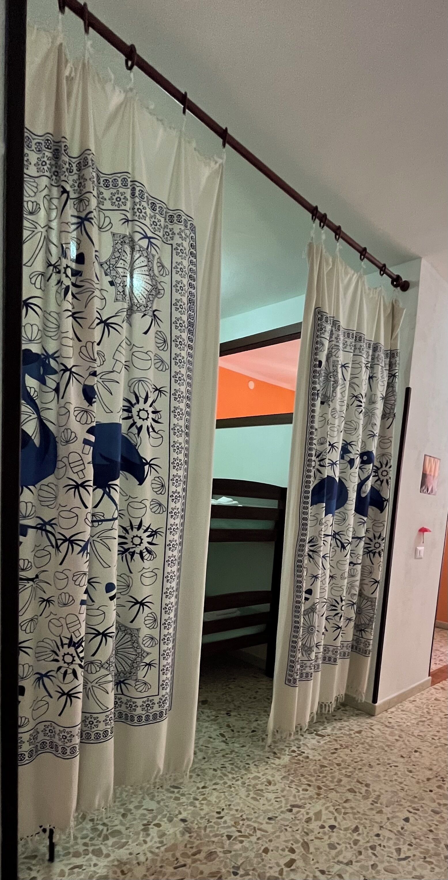 A corridor with patterned curtains, a bed, and a tiled floor.