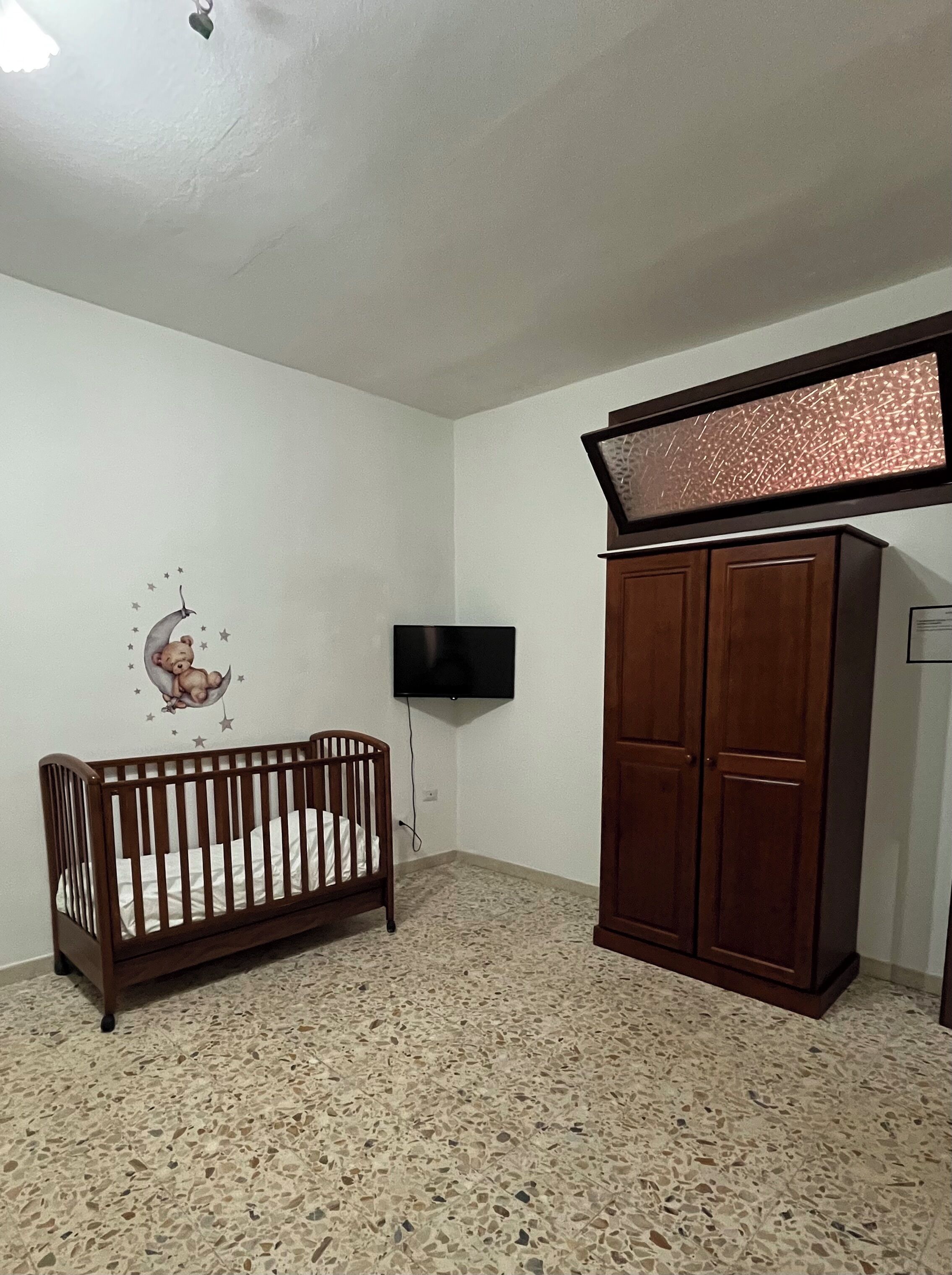 Ein Zimmer mit einem Kinderbett, einem Kleiderschrank, einem an der Wand befestigten Fernseher und einer Wanddekoration.